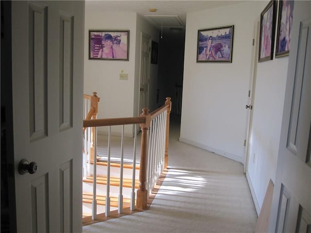 hall with attic access, an upstairs landing, light colored carpet, and baseboards