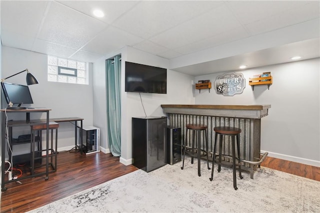 indoor dry bar featuring wood finished floors, baseboards, and a drop ceiling