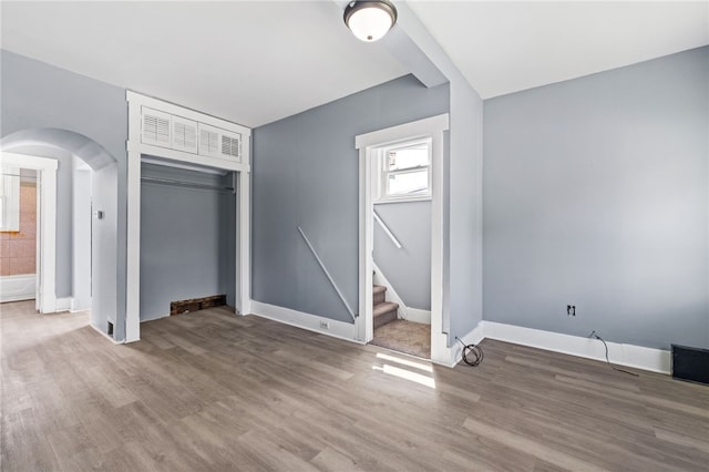 unfurnished living room featuring arched walkways, wood finished floors, stairs, and baseboards