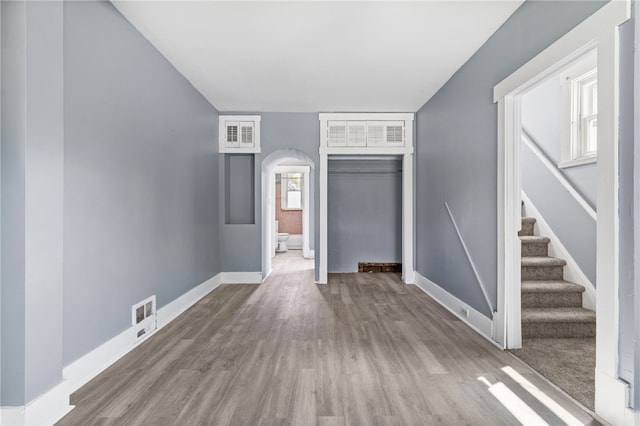 unfurnished living room featuring arched walkways, wood finished floors, baseboards, and stairs