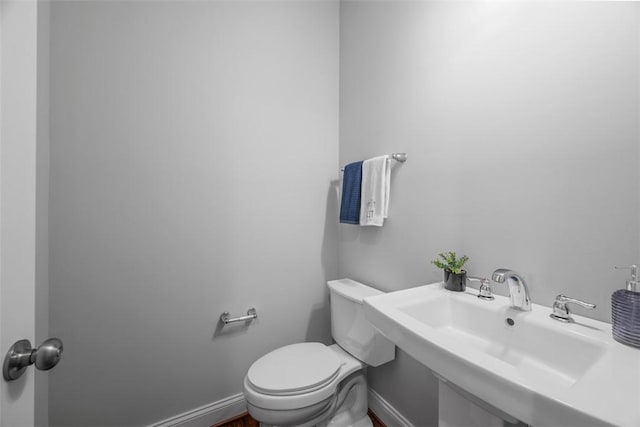 bathroom featuring toilet, baseboards, and a sink