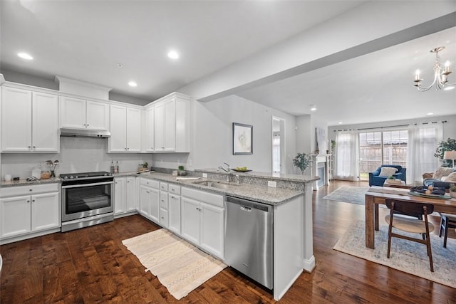 kitchen with appliances with stainless steel finishes, under cabinet range hood, a peninsula, open floor plan, and a chandelier