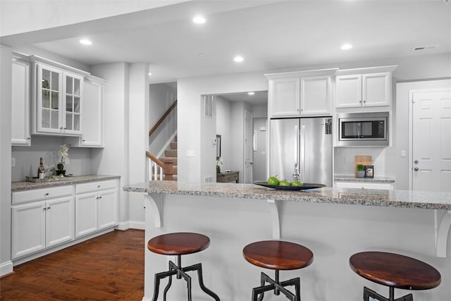 kitchen featuring stainless steel appliances, white cabinetry, a breakfast bar, glass insert cabinets, and recessed lighting