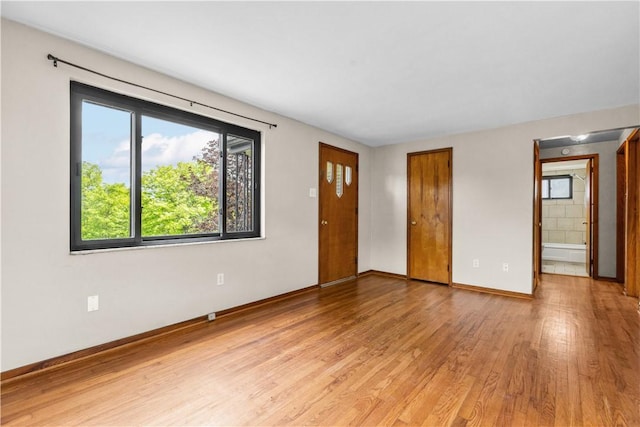 unfurnished living room featuring light wood finished floors, plenty of natural light, and baseboards