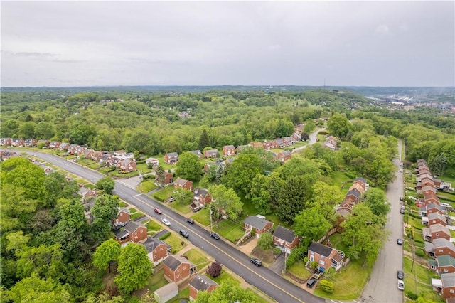 aerial view of property and surrounding area featuring a forest and nearby suburban area