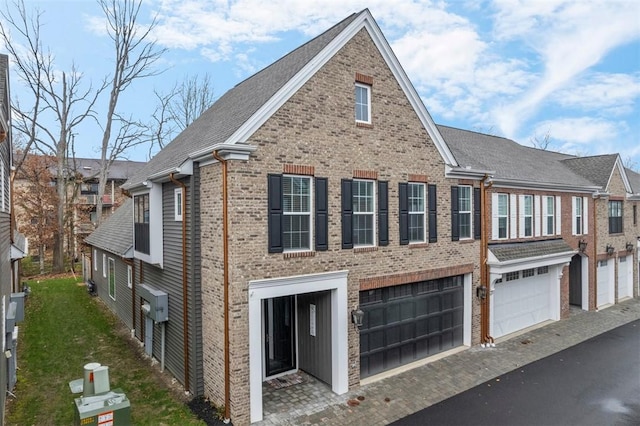 view of front of home featuring brick siding, driveway, an attached garage, and roof with shingles