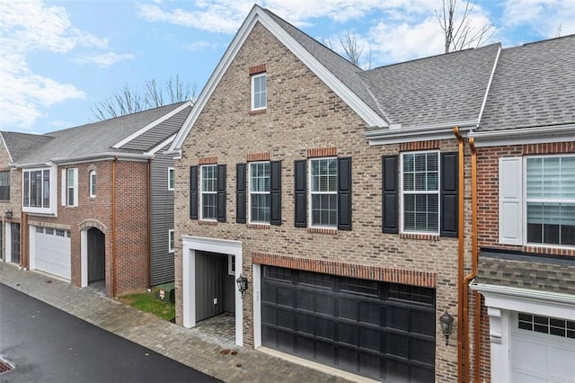 townhome / multi-family property with brick siding, a garage, and a shingled roof