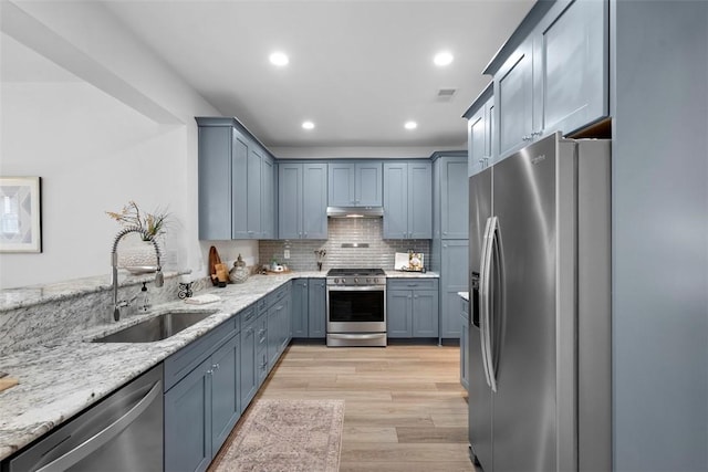 kitchen with stainless steel appliances, a sink, light stone countertops, recessed lighting, and light wood finished floors