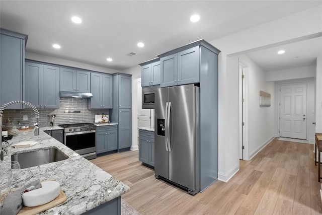kitchen featuring appliances with stainless steel finishes, a sink, light stone counters, light wood-style floors, and recessed lighting