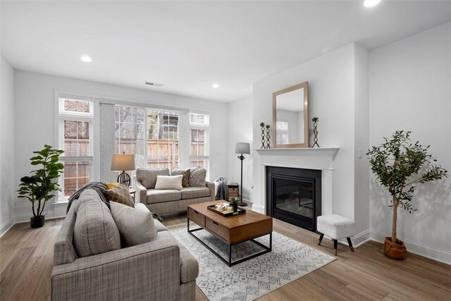 living area featuring light wood finished floors, baseboards, a glass covered fireplace, and recessed lighting