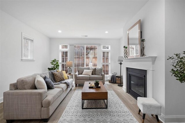 living room featuring a glass covered fireplace, light wood finished floors, baseboards, and recessed lighting
