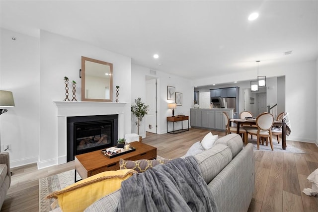 living area with light wood-style flooring, baseboards, a glass covered fireplace, and recessed lighting
