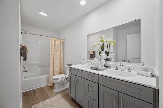 bathroom featuring wood finished floors, toilet, double vanity, and shower / bath combo with shower curtain