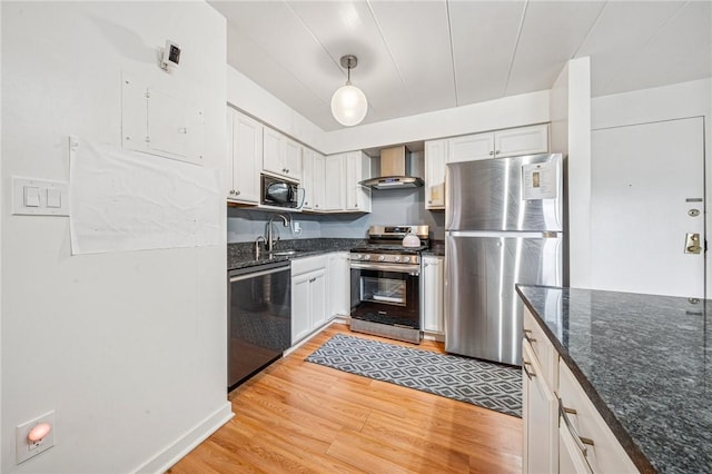 kitchen featuring stainless steel appliances, wall chimney exhaust hood, light wood finished floors, a sink, and dark stone countertops