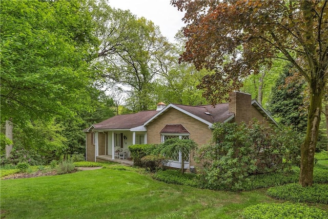 ranch-style home featuring a chimney, a front lawn, a porch, and brick siding