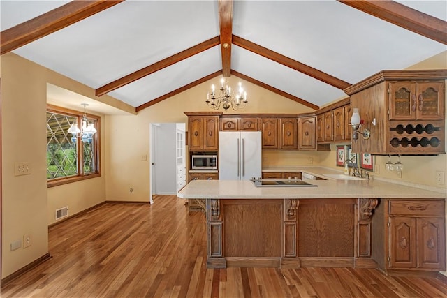 kitchen with a chandelier, freestanding refrigerator, stainless steel microwave, a sink, and light countertops