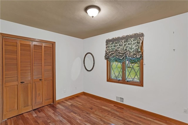 unfurnished bedroom featuring wood finished floors, baseboards, and a closet