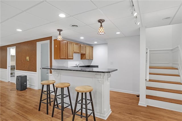 kitchen featuring a breakfast bar, light wood finished floors, decorative light fixtures, wainscoting, and a peninsula