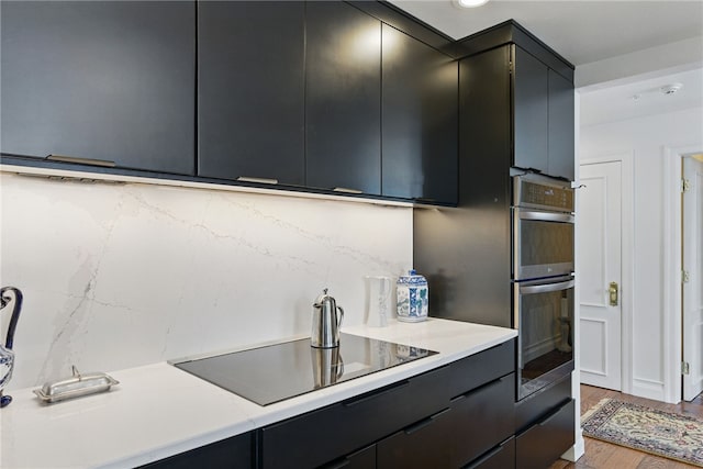 kitchen featuring black electric stovetop, dark cabinets, double oven, and light countertops