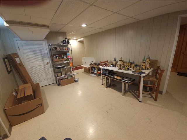 finished basement featuring tile patterned floors, wooden walls, and a drop ceiling