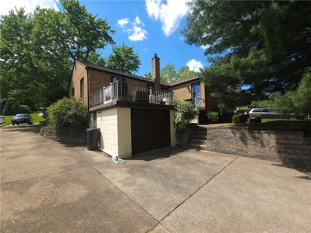 view of front facade featuring driveway, a balcony, a chimney, a garage, and brick siding