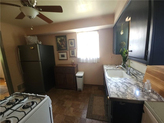 kitchen with freestanding refrigerator, gas range gas stove, light countertops, a ceiling fan, and a sink
