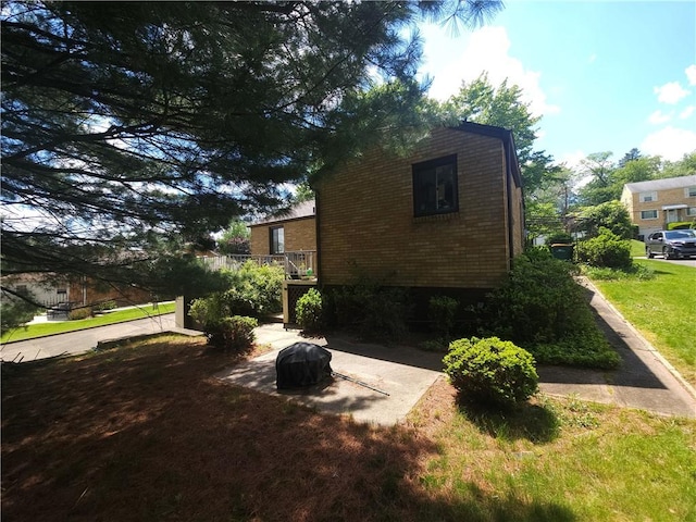 view of side of home with brick siding, a yard, and a wooden deck