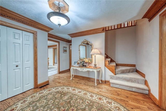 entryway featuring stairs, wood finished floors, baseboards, a textured ceiling, and ornamental molding