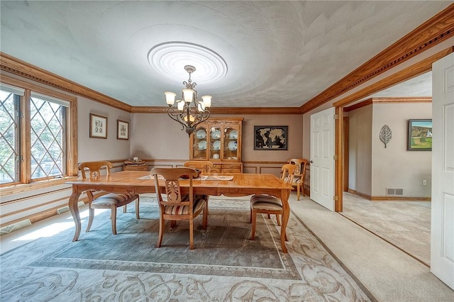dining space featuring light carpet, a chandelier, crown molding, and a wainscoted wall