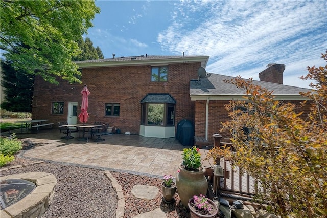 back of house with brick siding, a patio, a chimney, and a shingled roof