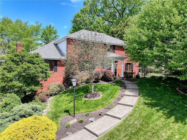view of front of property featuring brick siding, a front yard, a chimney, and roof with shingles