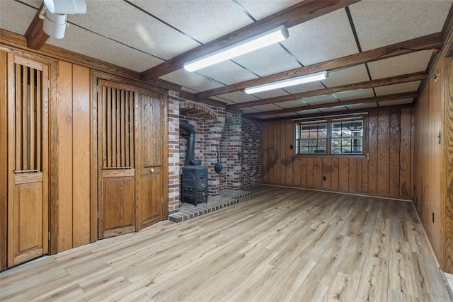 unfurnished room with wood walls, light wood-type flooring, and a wood stove