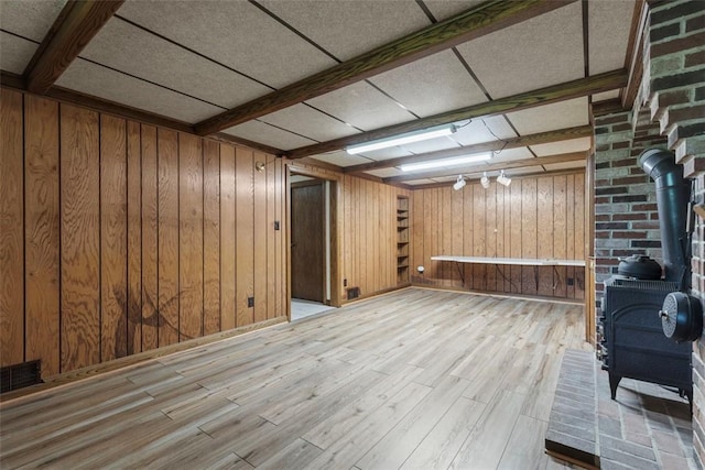 finished below grade area featuring a wood stove, wooden walls, and light wood finished floors