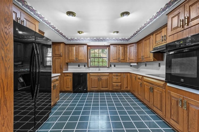kitchen with black appliances, brown cabinetry, dark tile patterned flooring, under cabinet range hood, and light countertops