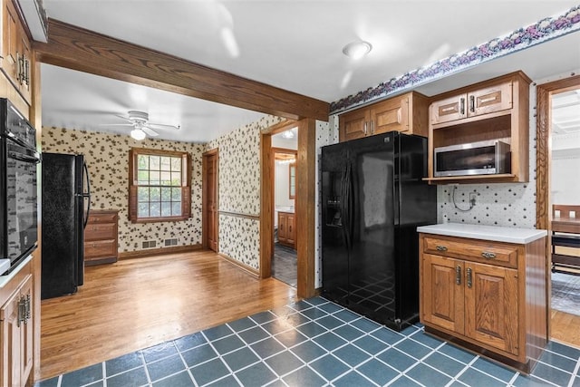 kitchen with black appliances, wallpapered walls, a ceiling fan, dark wood-style floors, and light countertops