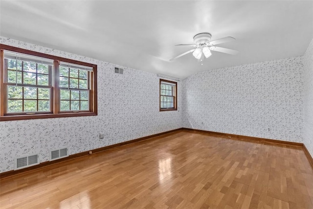 empty room with healthy amount of natural light, light wood finished floors, wallpapered walls, and ceiling fan