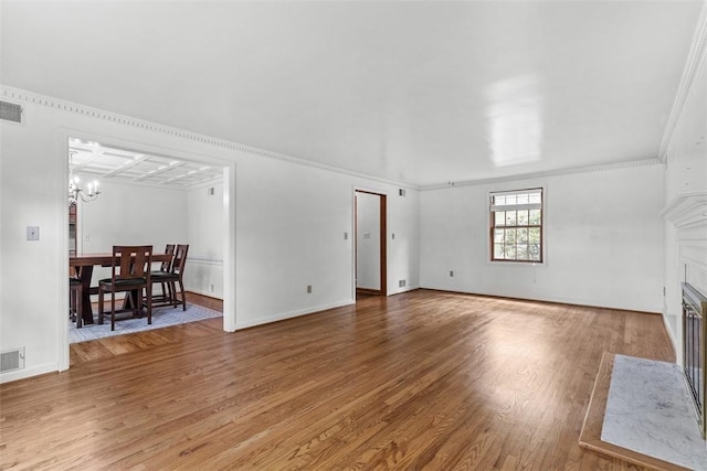 living room featuring a chandelier, a fireplace with flush hearth, wood finished floors, ornamental molding, and baseboards