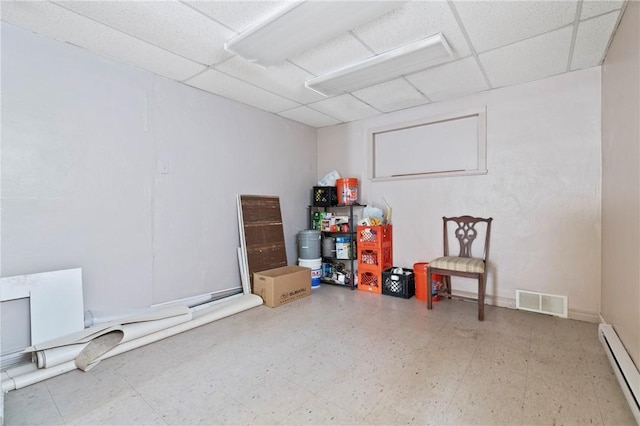 basement featuring a baseboard radiator, tile patterned floors, and a drop ceiling