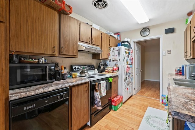 kitchen with black appliances, under cabinet range hood, a sink, light wood finished floors, and decorative backsplash