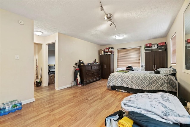 bedroom with a textured ceiling, light wood-style floors, and baseboards