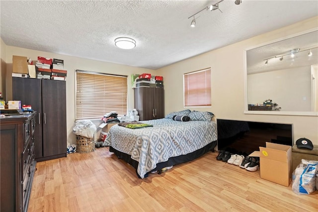 bedroom with track lighting, light wood finished floors, and a textured ceiling