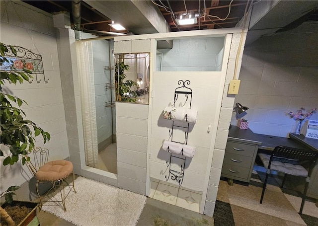 full bath featuring a tile shower, concrete block wall, and concrete flooring