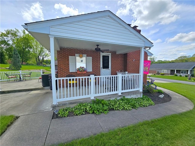bungalow-style house with a porch, a ceiling fan, a chimney, brick siding, and a front lawn