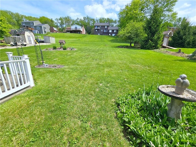 view of grassy yard featuring a residential view, a shed, and an outdoor structure