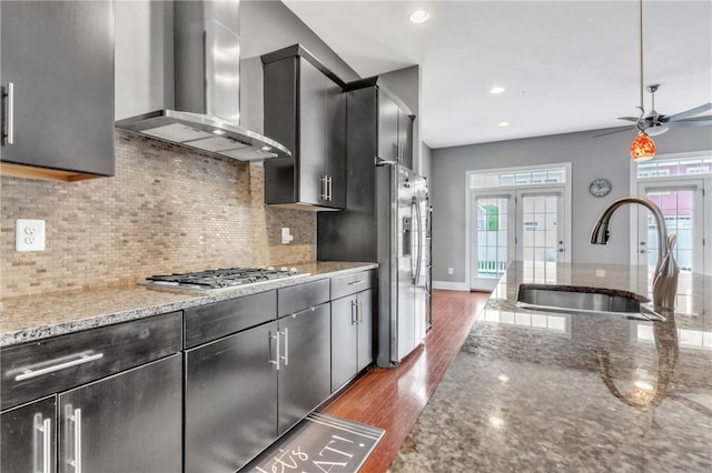 kitchen with wall chimney exhaust hood, a sink, stainless steel appliances, dark wood-style floors, and a ceiling fan