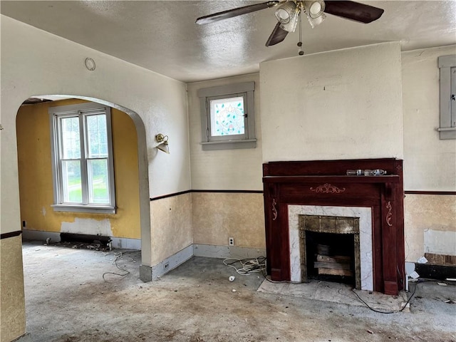 unfurnished living room with ceiling fan, arched walkways, plenty of natural light, a high end fireplace, and a textured ceiling