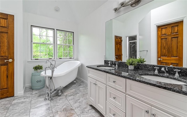 bathroom with baseboards, a shower stall, vaulted ceiling, a freestanding bath, and double vanity