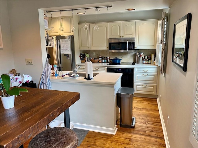 kitchen featuring black appliances, light wood-type flooring, baseboards, a sink, and light countertops
