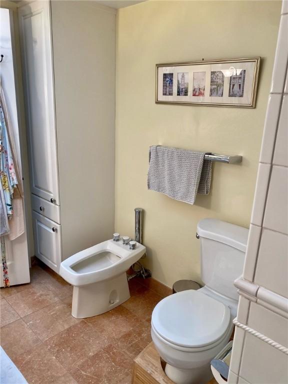 bathroom with toilet, a bidet, and stone finish flooring