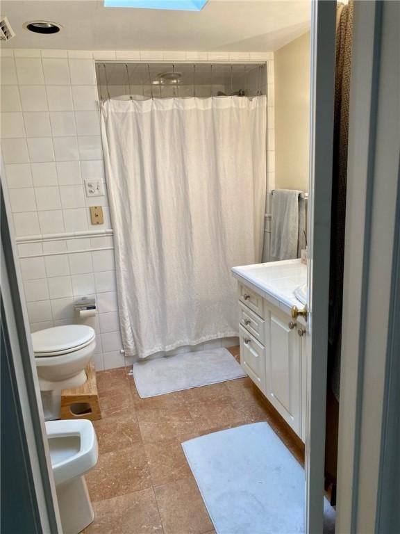 full bathroom with tile walls, toilet, a shower with shower curtain, vanity, and a skylight